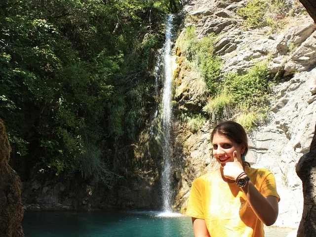 A person giving a thumbs-up in front of a waterfall.